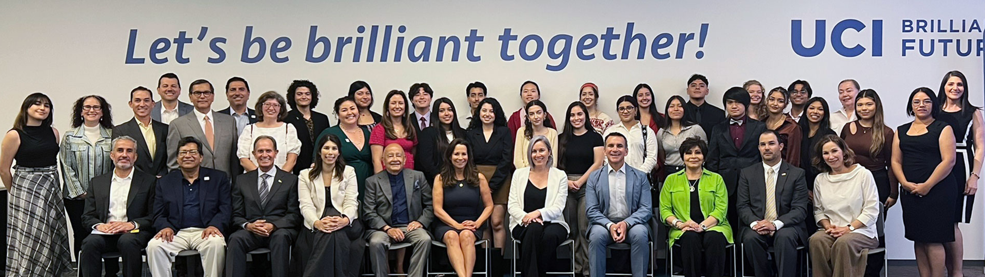 UCI-OC Alliance members in front of a sign that says "Let's be brilliant together!"